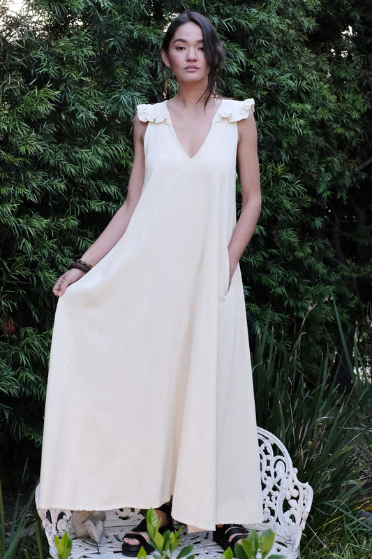 Woman in an alabaster dress standing outdoors with greenery in the background