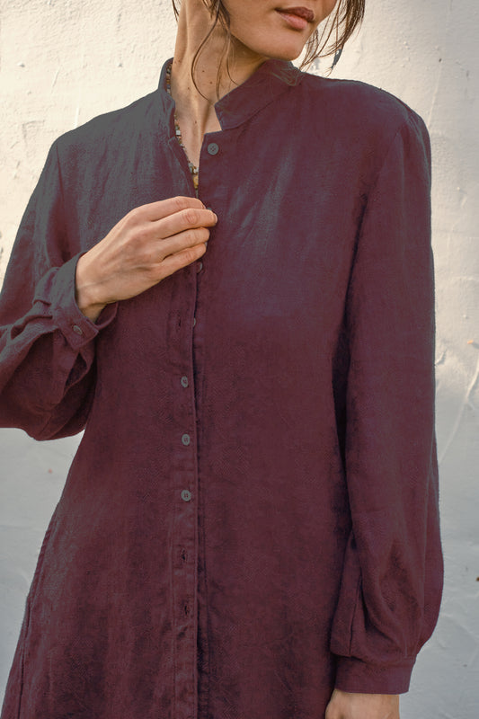 Detail of a person wearing a burgundy button-up damask coat against a neutral background