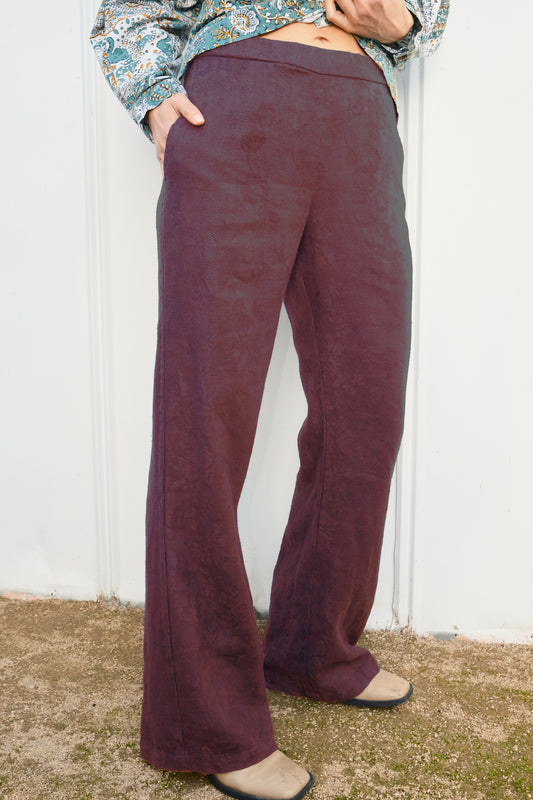 Person wearing maroon flared pants against a white wall.