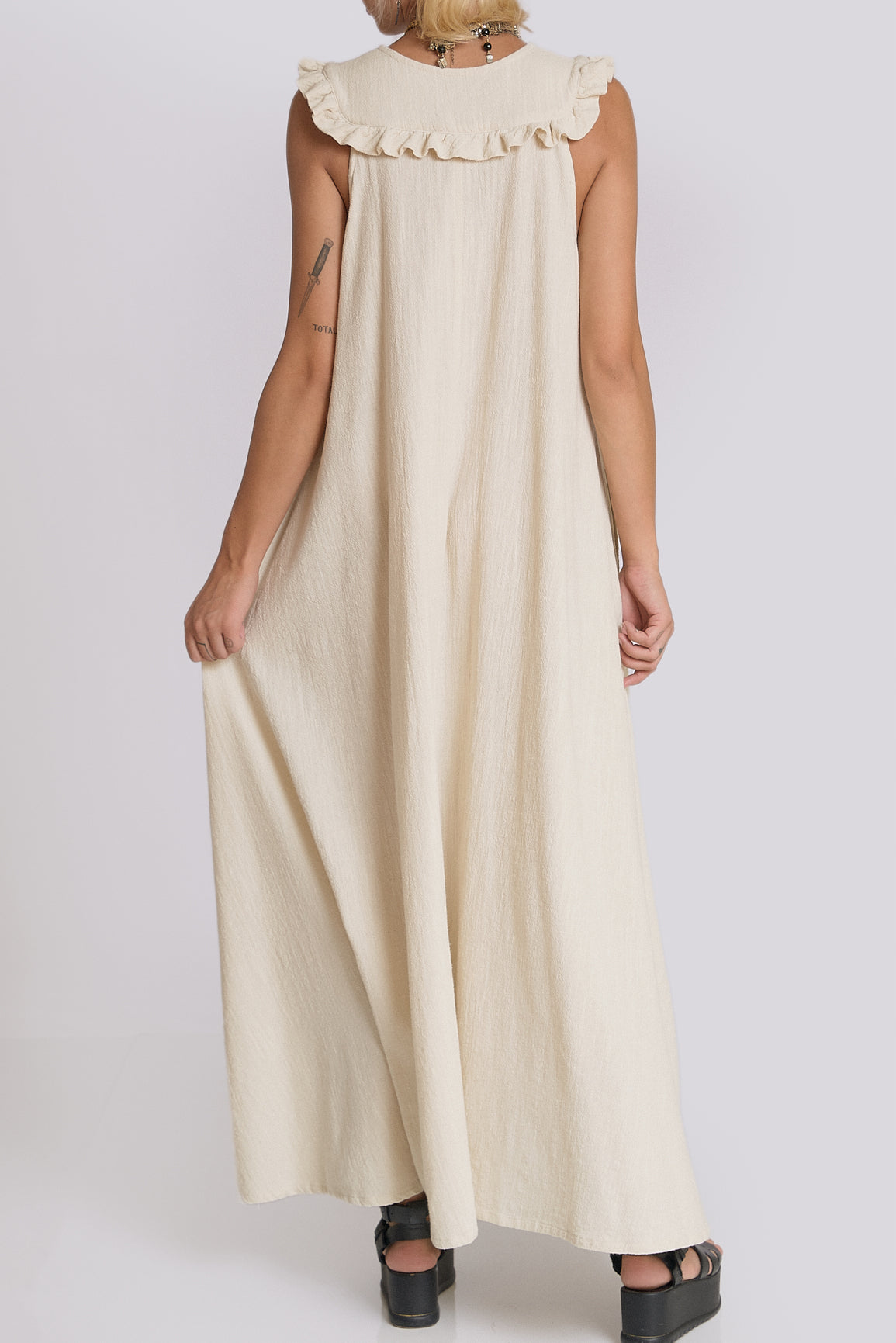 Woman wearing a long beige dress with a ruffled collar on a white background