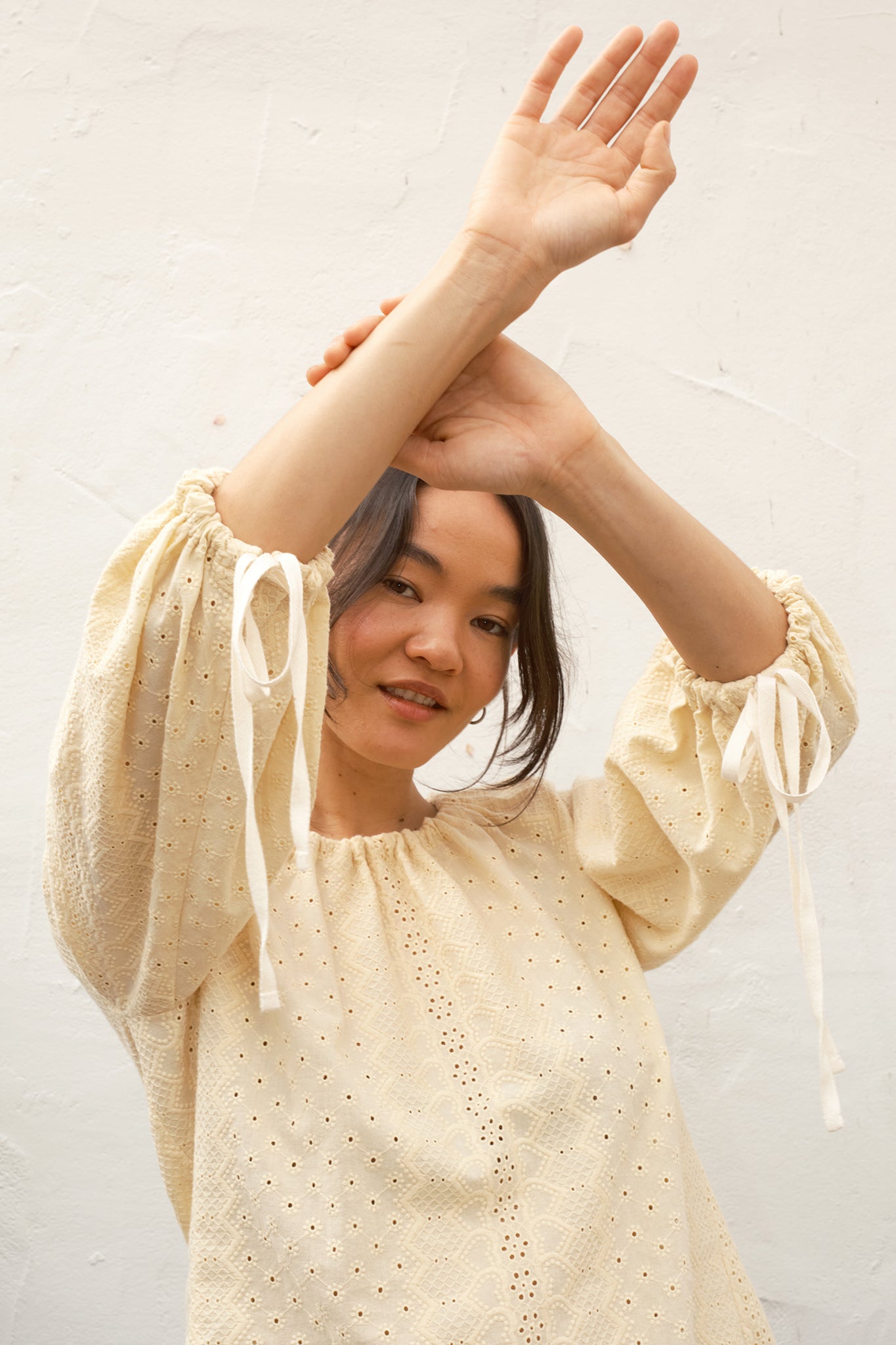 Woman wearing a beige blouse with long sleeves and a white background