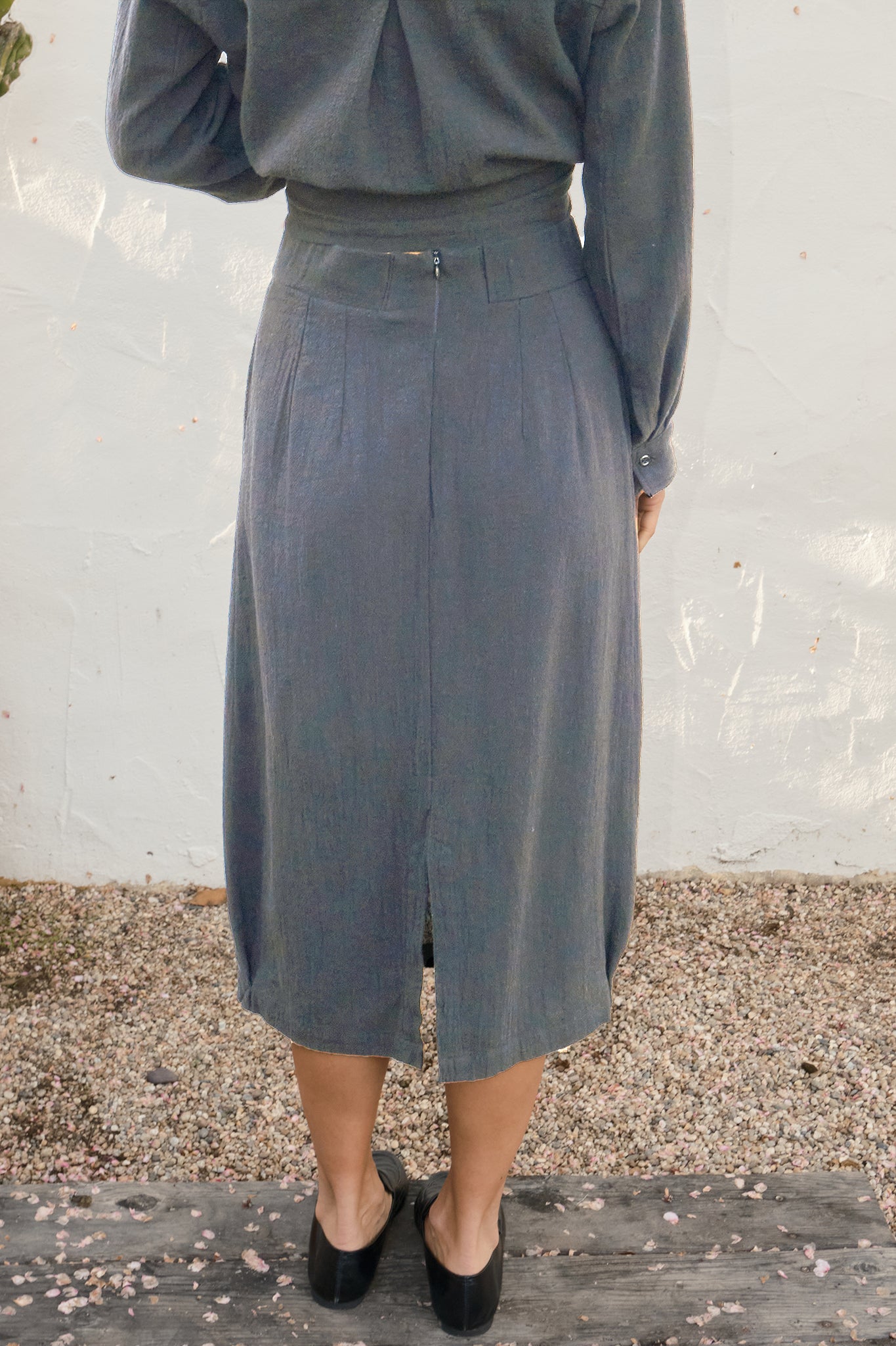 Person wearing a gray skirt and top against a white wall.