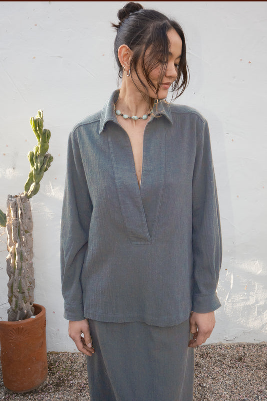 Woman wearing a gray outfit standing next to a cactus plant against a white wall.