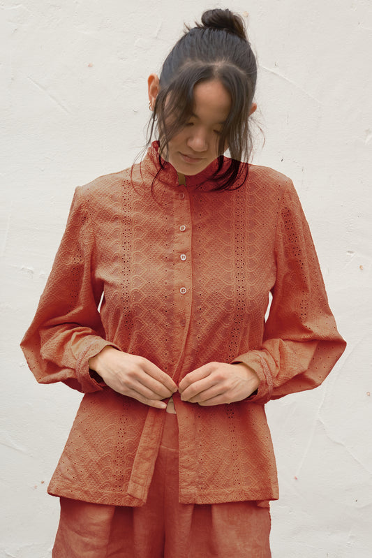 Person wearing a rust-colored embroidered blouse against a white background