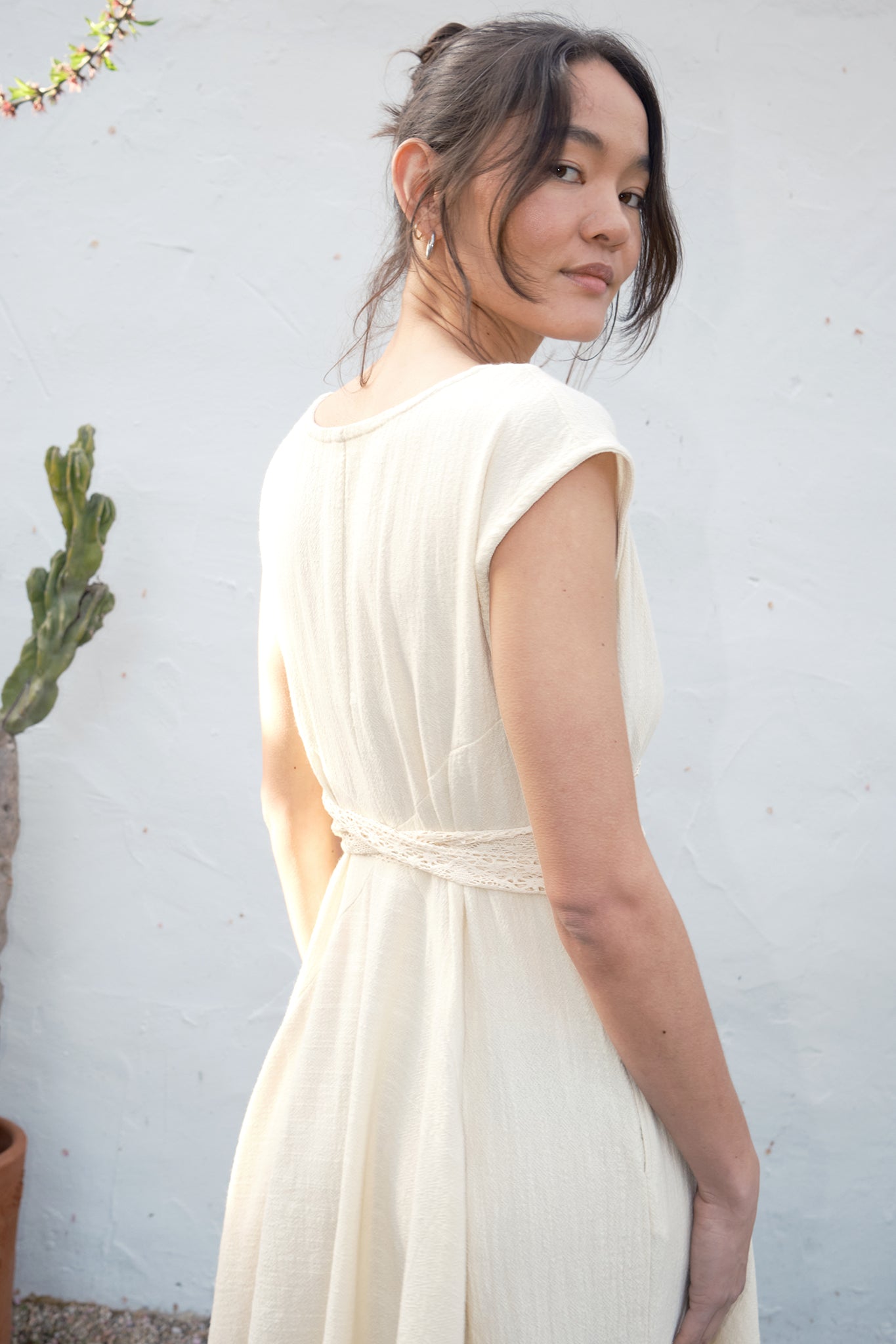 Woman wearing an alabaster dress against a light gray wall with a plant in the background