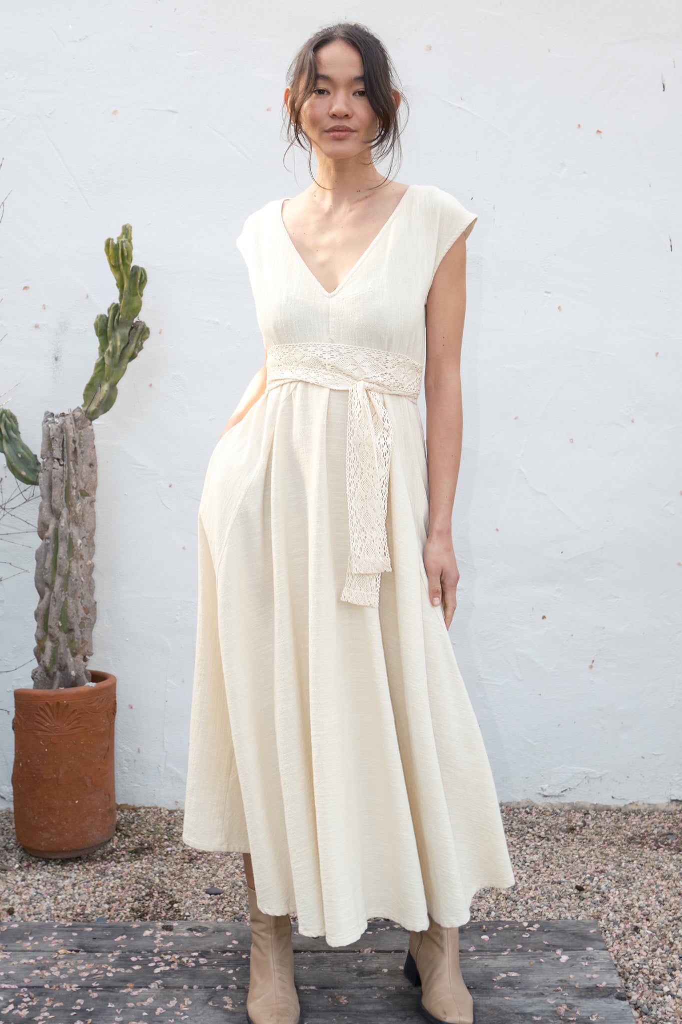 Woman wearing an alabaster dress standing against a white wall with a cactus plant.
