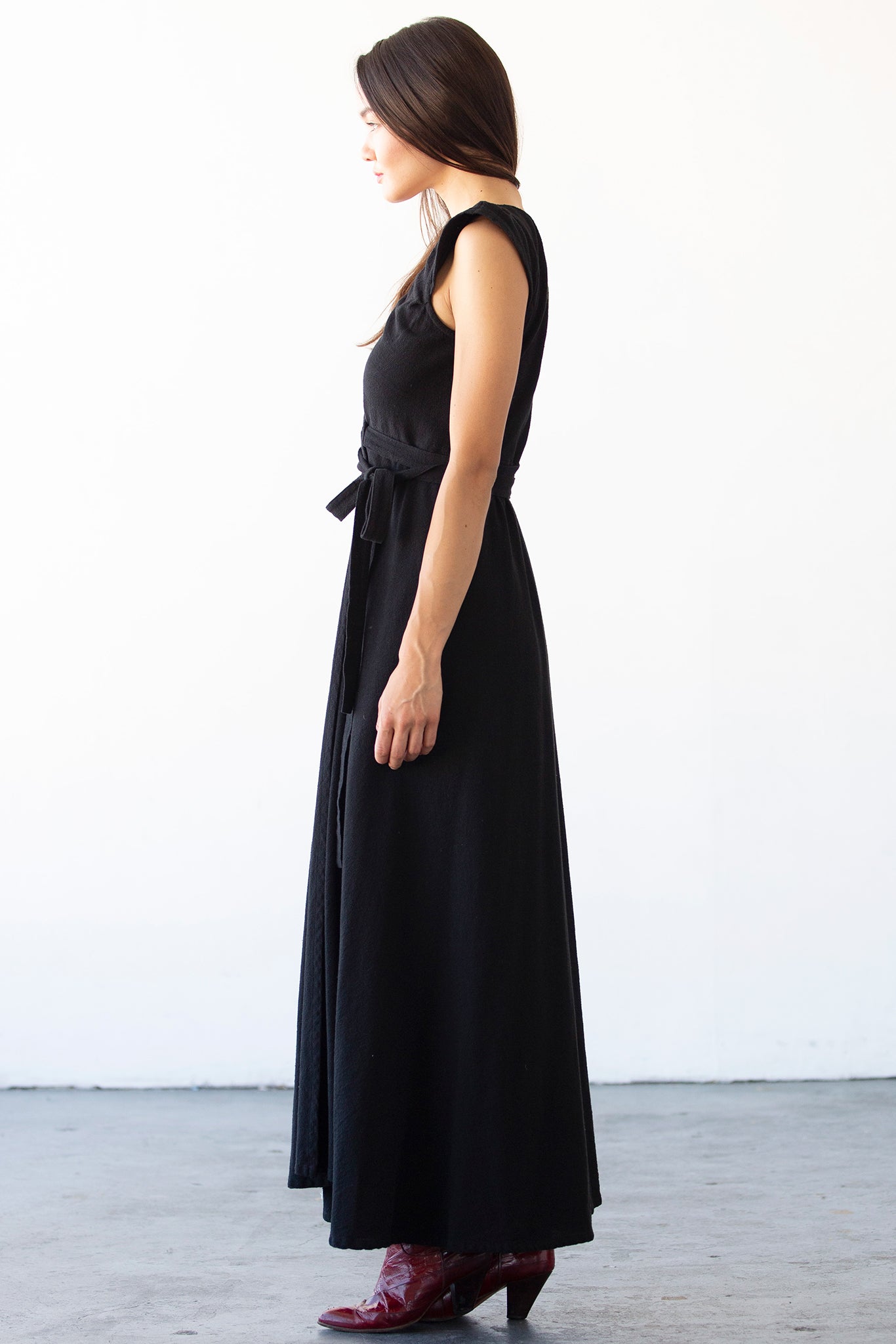 Woman wearing a black dress with a belt, standing against a white background.