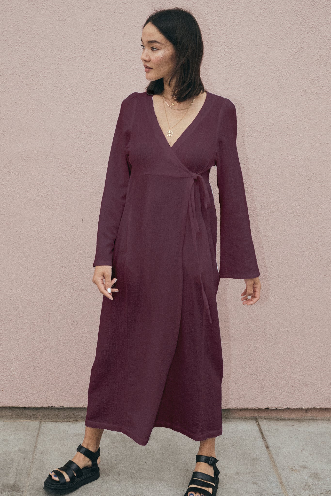 Woman wearing a purple wrap dress against a pink wall.