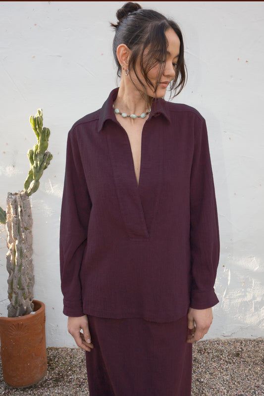 Woman wearing a burgundy outfit standing against a white wall with a cactus plant.