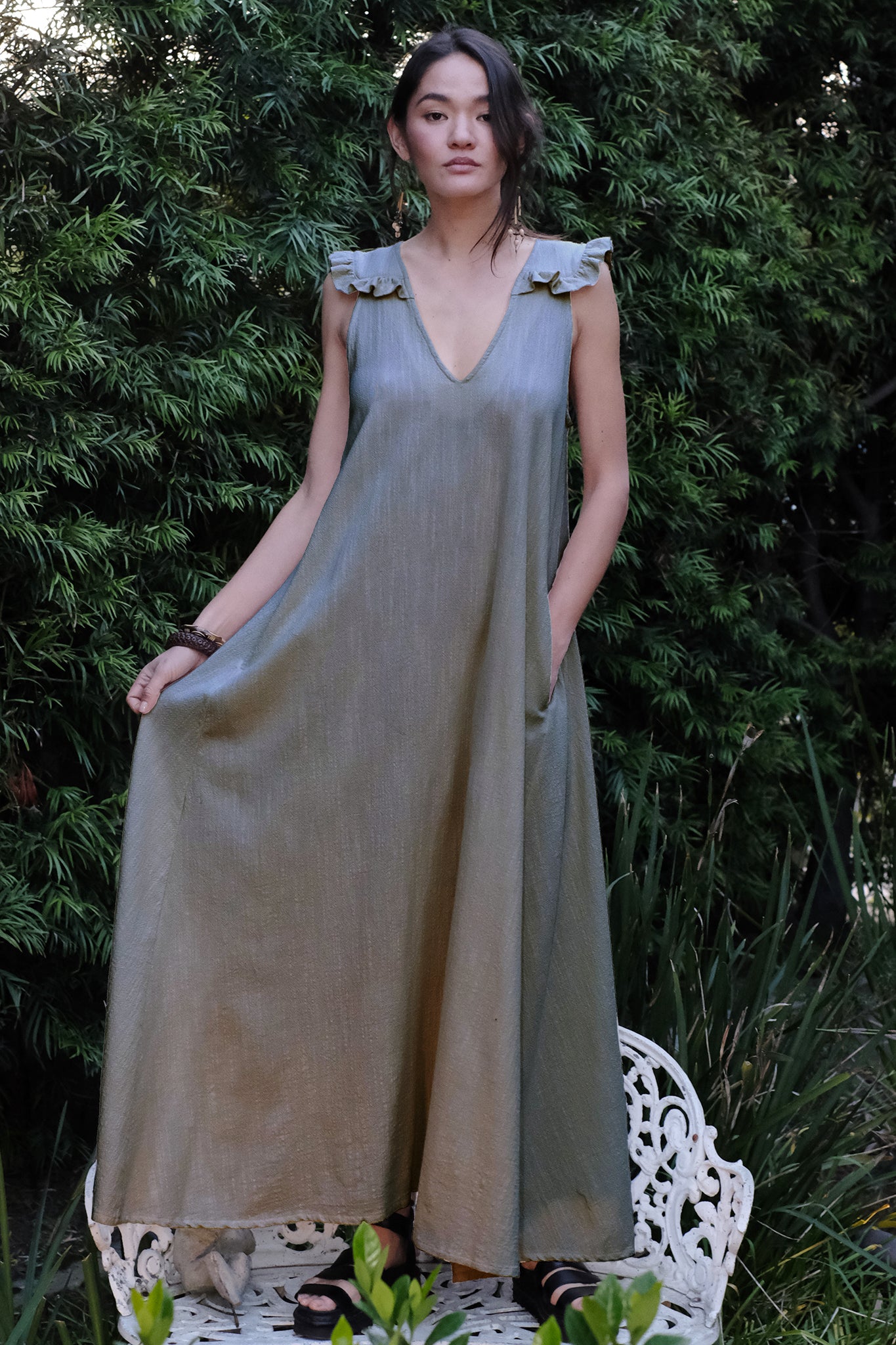 woman standing on bench in garden wearing a grey colored long dress.
