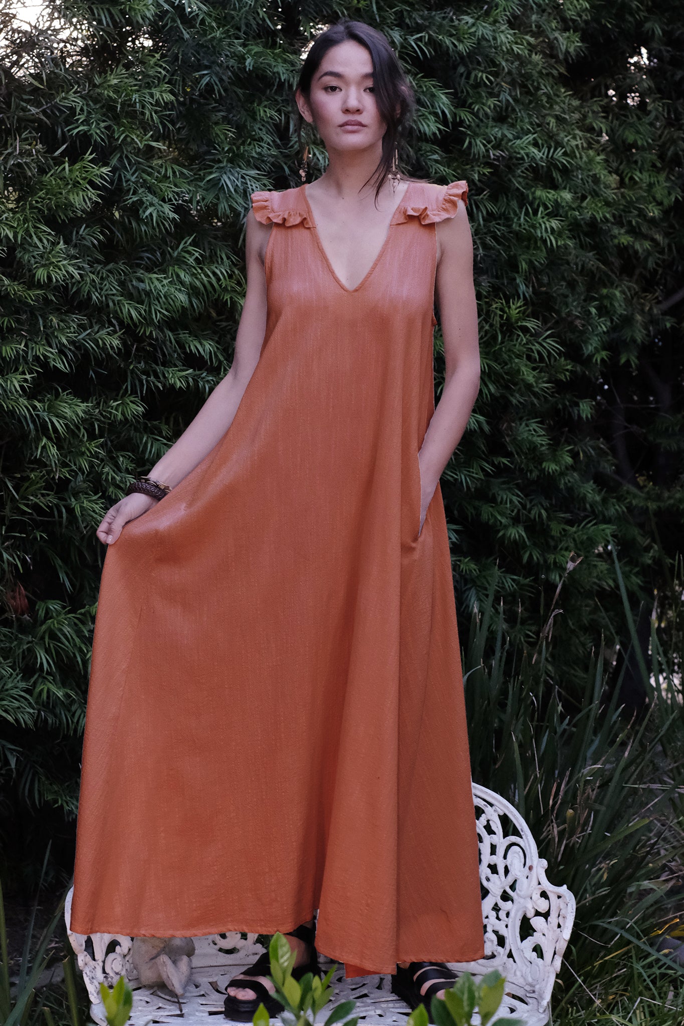 woman standing on bench in garden wearing a persimmon colored long dress.