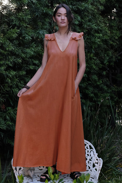 Woman wearing an orange dress standing on a white chair with greenery in the background