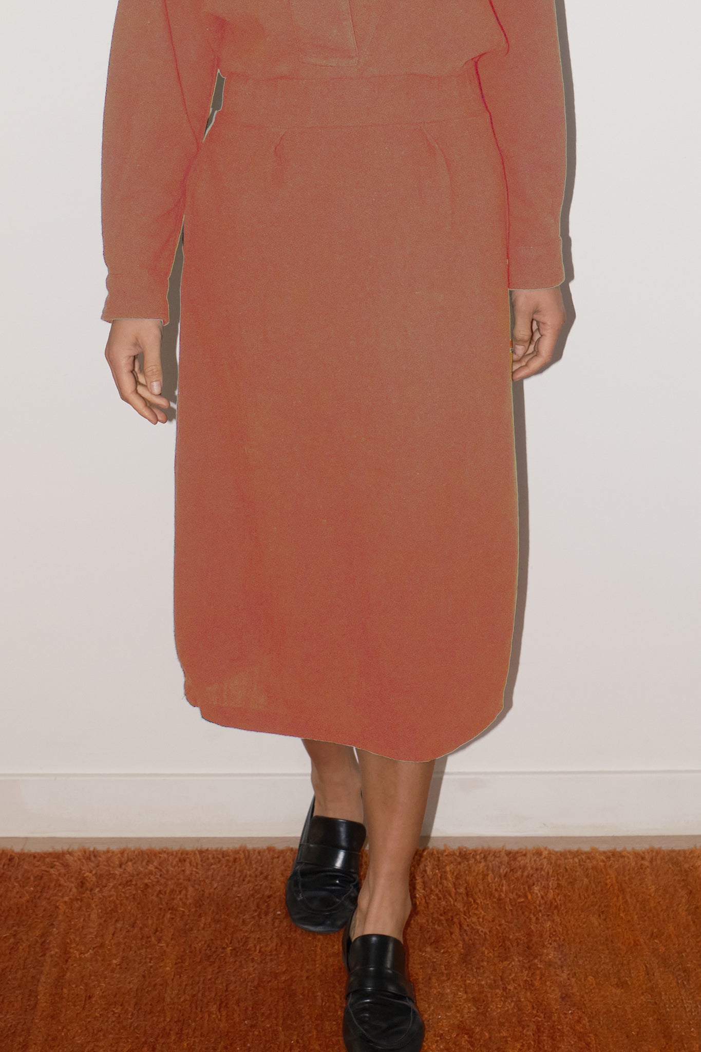 Person wearing a rust-colored skirt with black shoes on a plain background