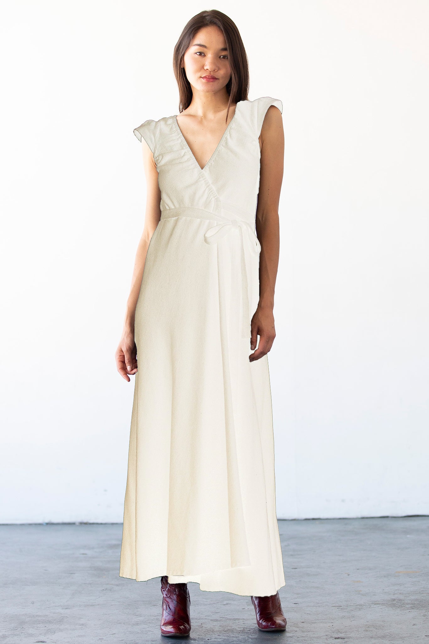 Woman wearing a long alabaster dress with ruffled sleeves against a white background