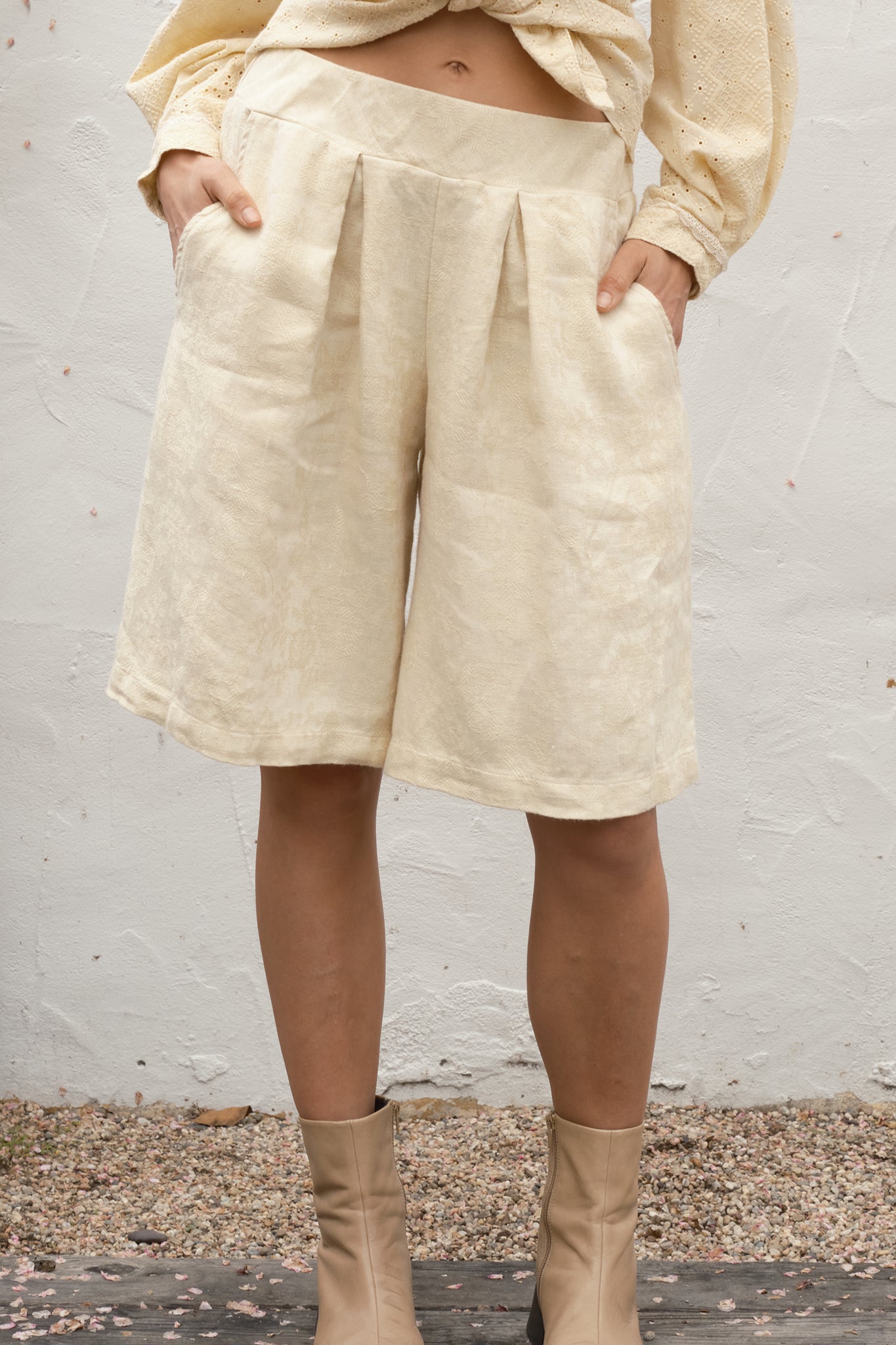Person wearing alabaster shorts and boots against a white wall.