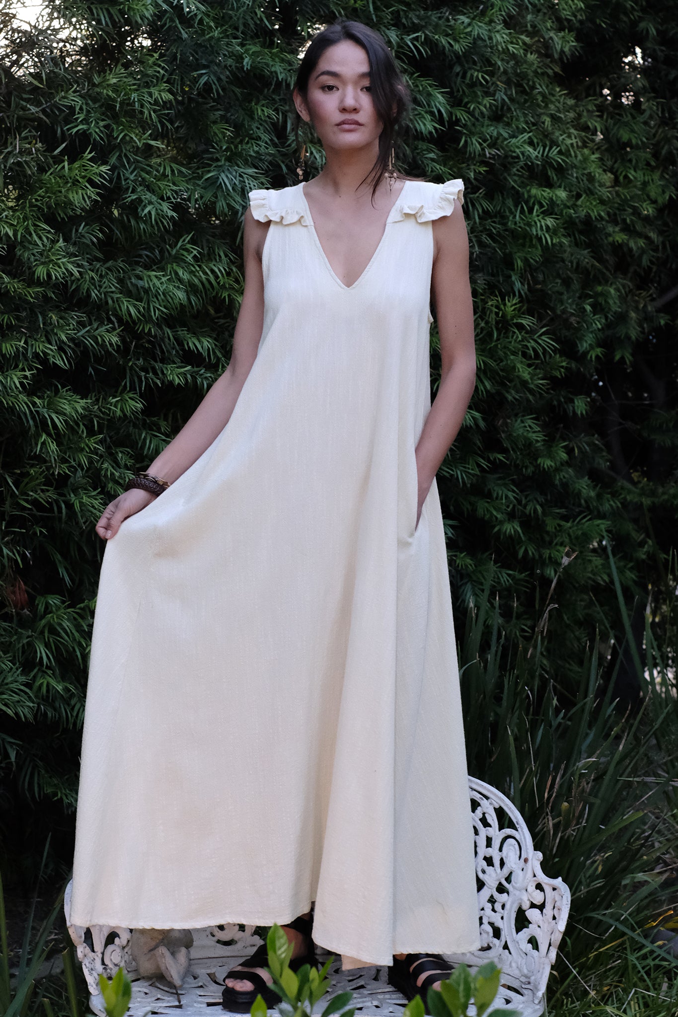 Woman wearing a white dress standing outdoors with greenery in the background