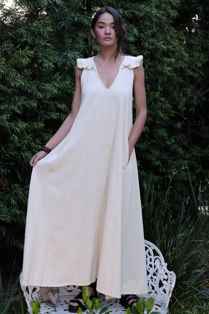 Woman wearing a white dress standing outdoors with greenery in the background