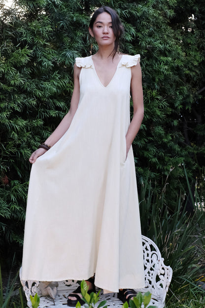 Woman in an alabaster  dress standing outdoors with greenery in the background