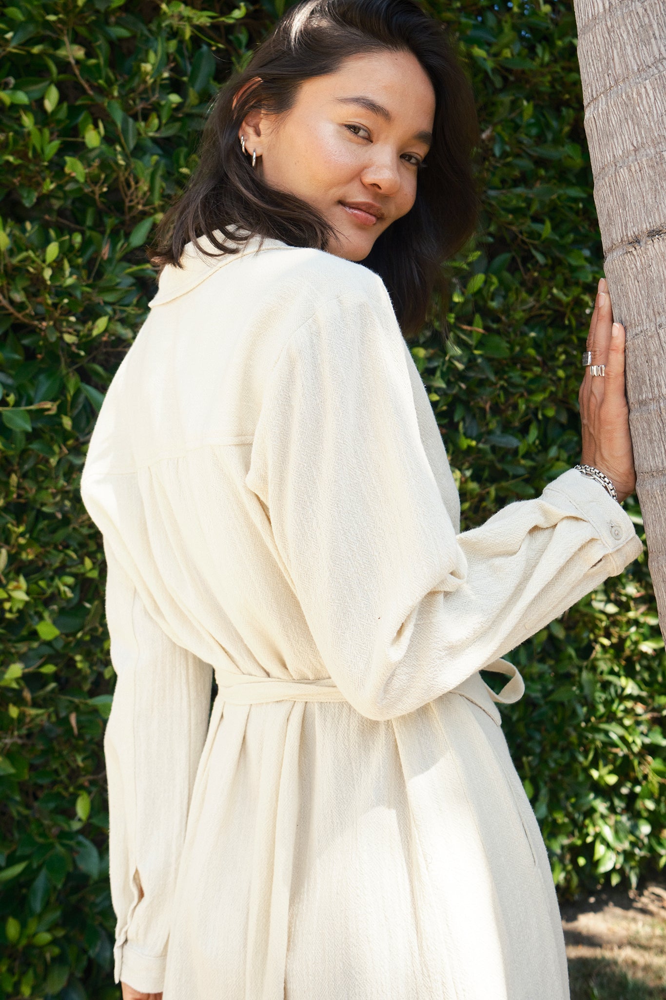 Woman in a cream-colored dress standing outdoors with greenery in the background
