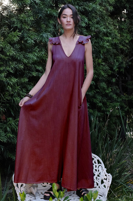 woman standing on bench in garden waring a fig colored long dress.