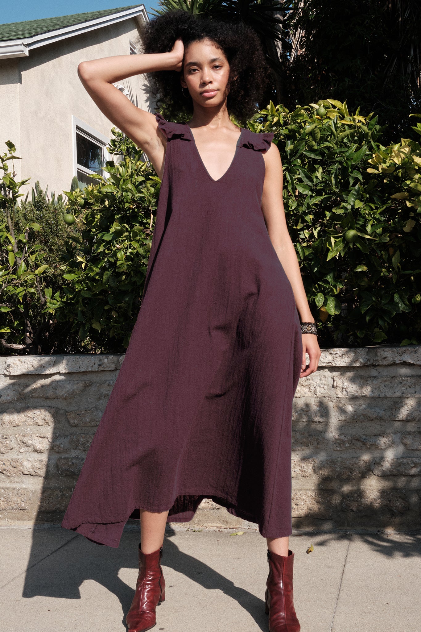 Woman wearing a burgundy dress standing outdoors with greenery in the background