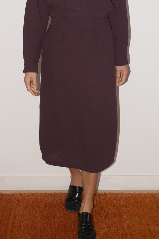 Person wearing a dark purple skirt with black shoes on a plain background