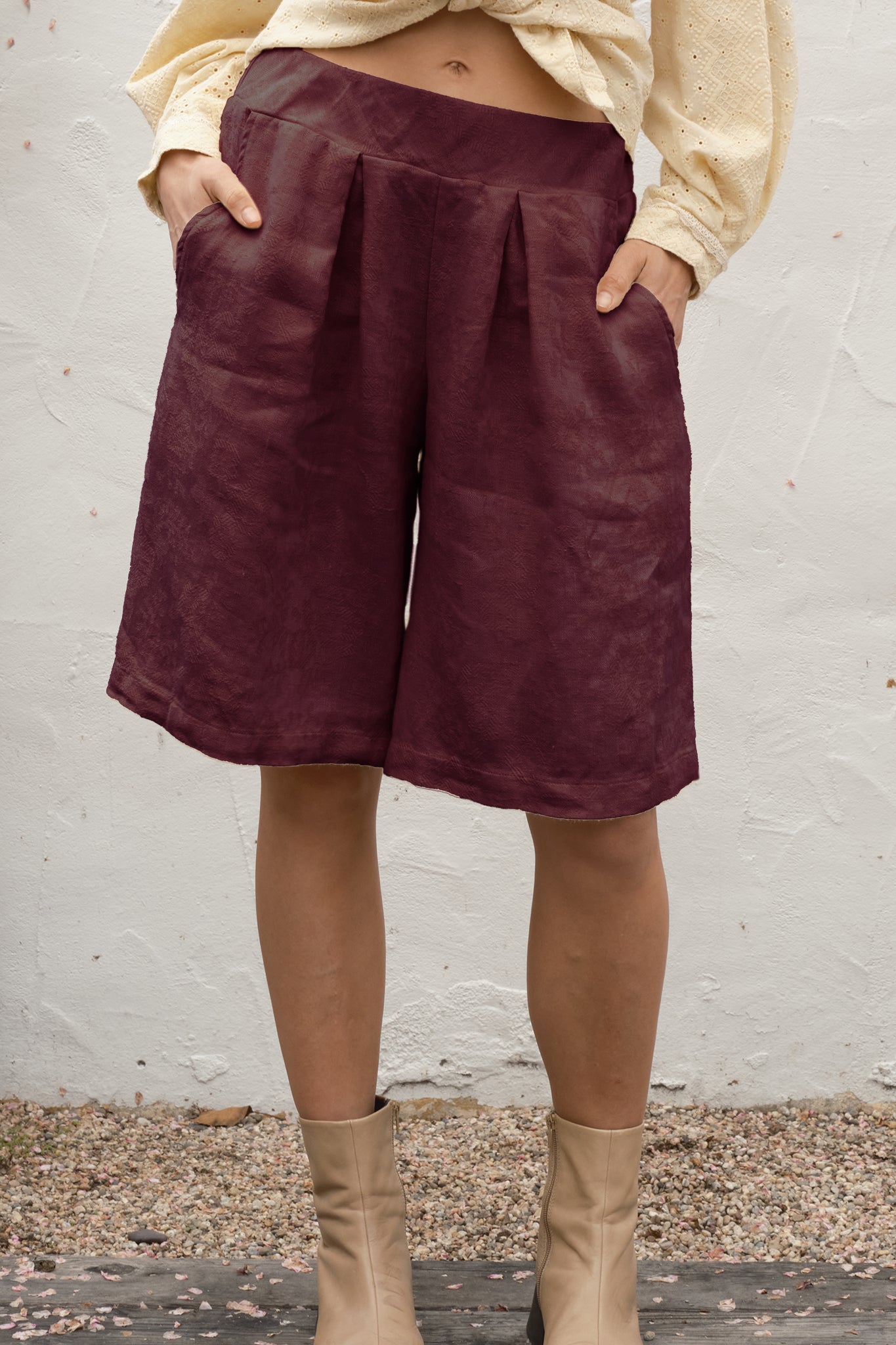 Person wearing maroon shorts and beige boots against a white wall.