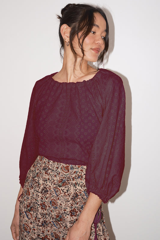 Woman wearing a burgundy blouse with long sleeves and a patterned skirt against a white background