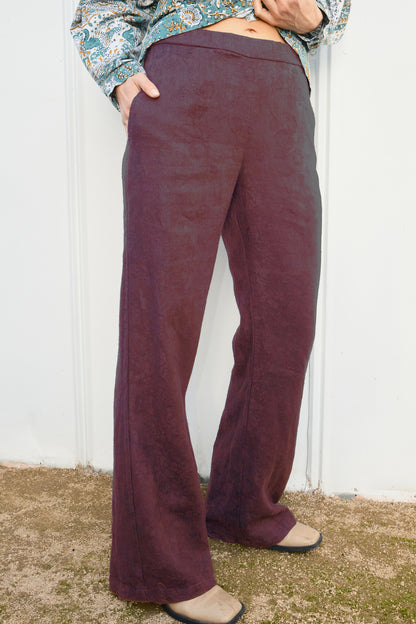 Person wearing maroon flared pants against a white wall.