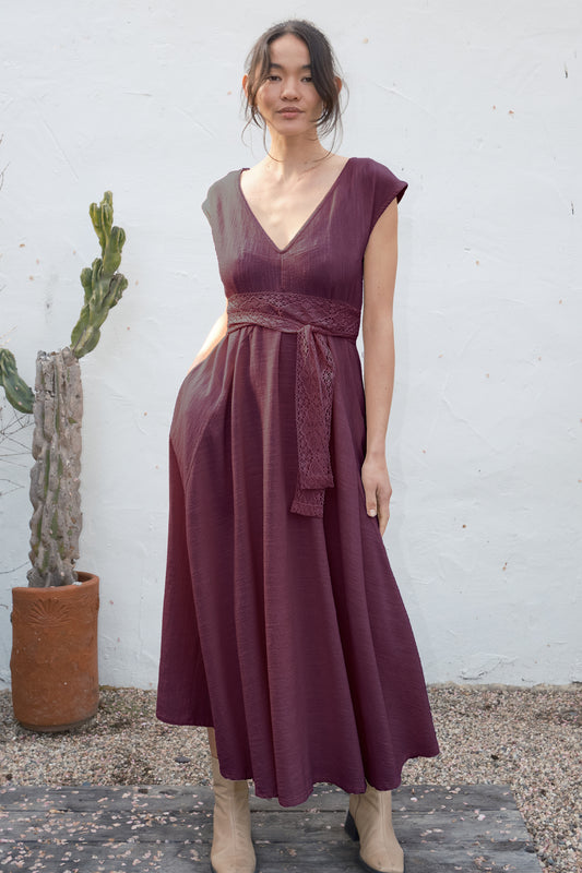 Woman wearing a burgundy dress standing against a white wall with a cactus plant.