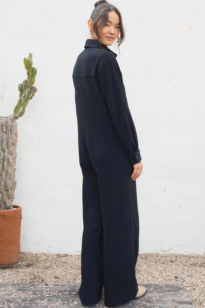 Person wearing a black outfit standing against a white wall with a cactus plant.