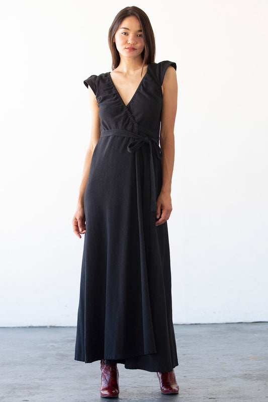 Woman wearing a black dress with ruffled shoulders against a white background