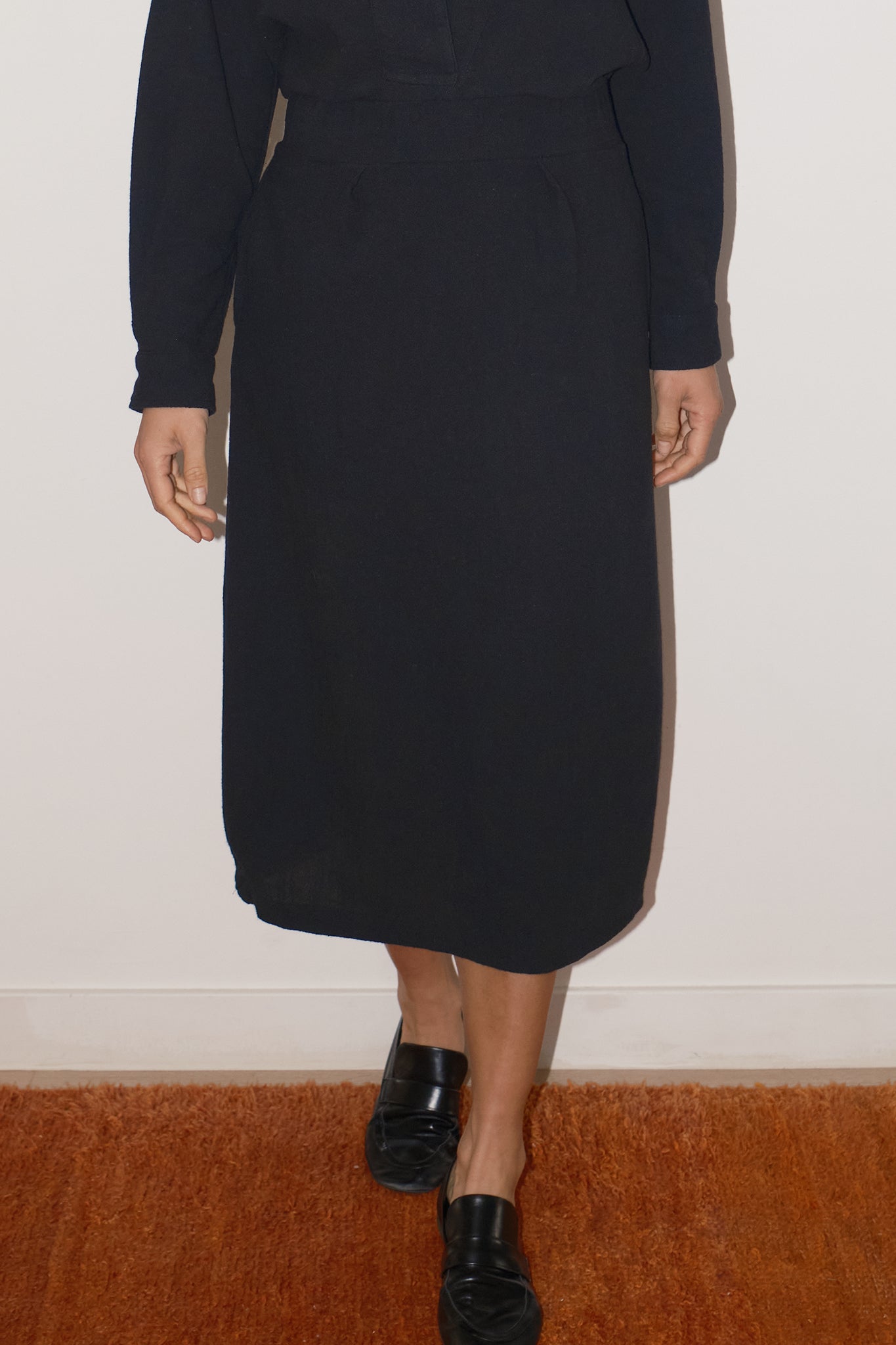 Person wearing a long black skirt with a plain background