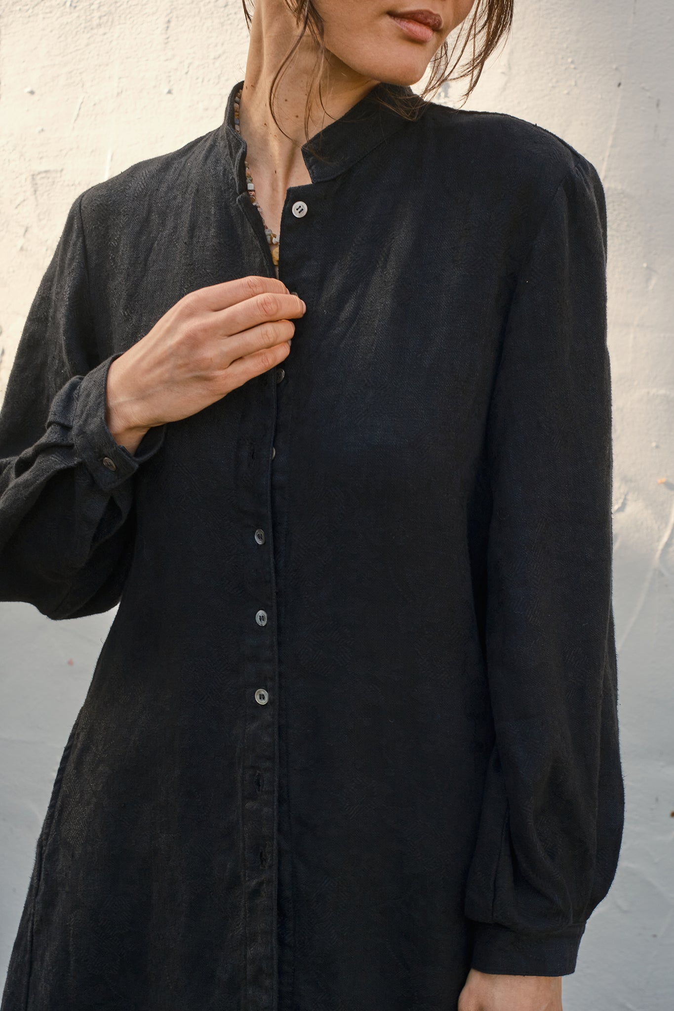 Detail of a person wearing a black button-up coat against a neutral background