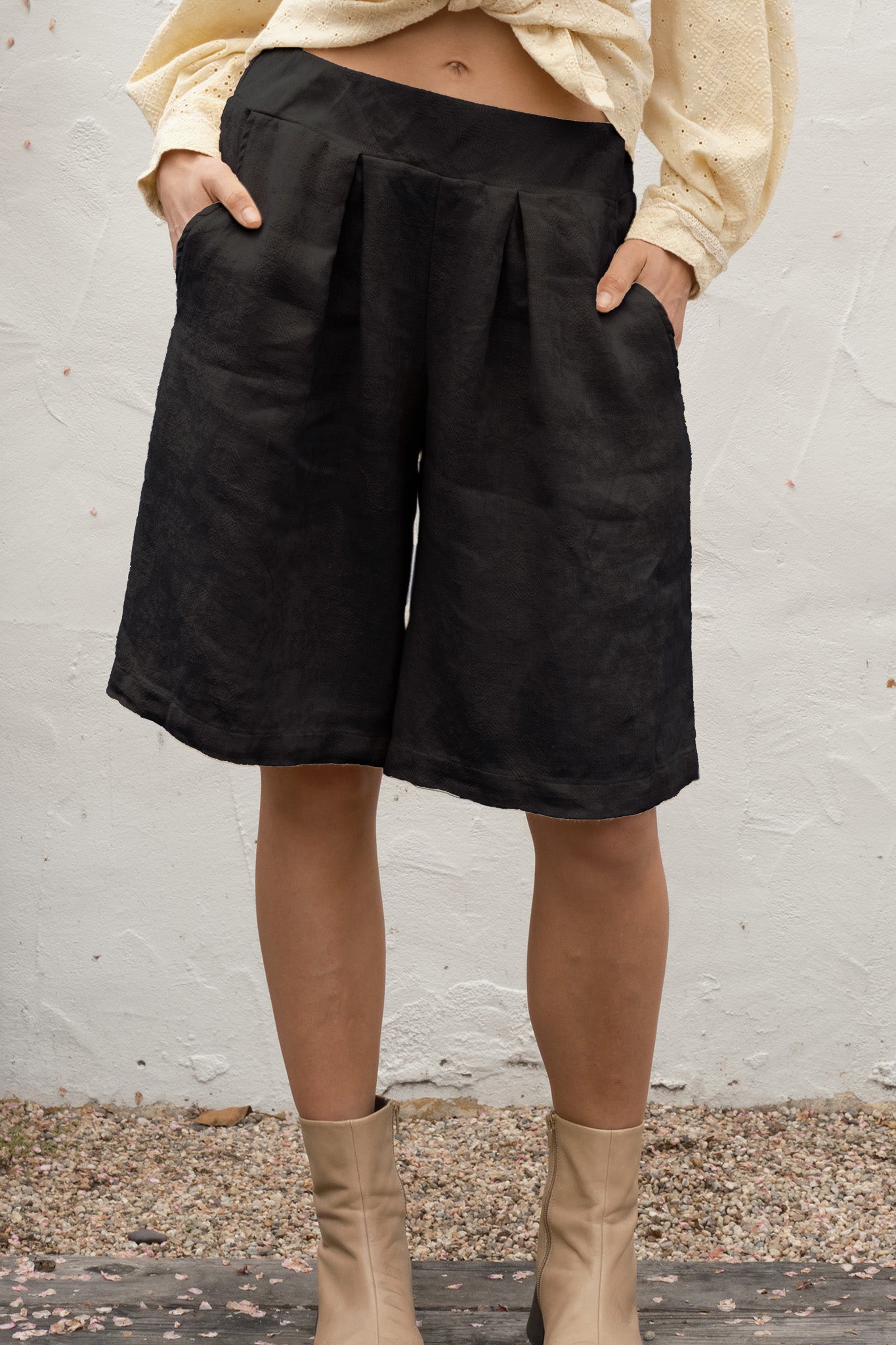 Person wearing black shorts and beige boots against a white wall.