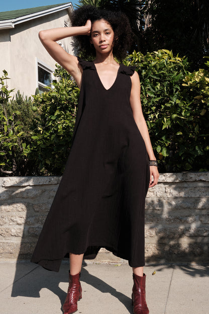 Woman wearing a black sleeveless dress with a deep neckline, standing outdoors.