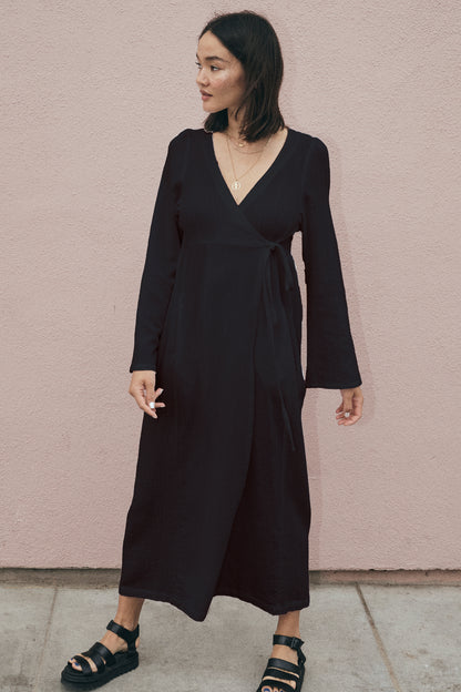 Woman wearing a black dress standing against a pink wall.
