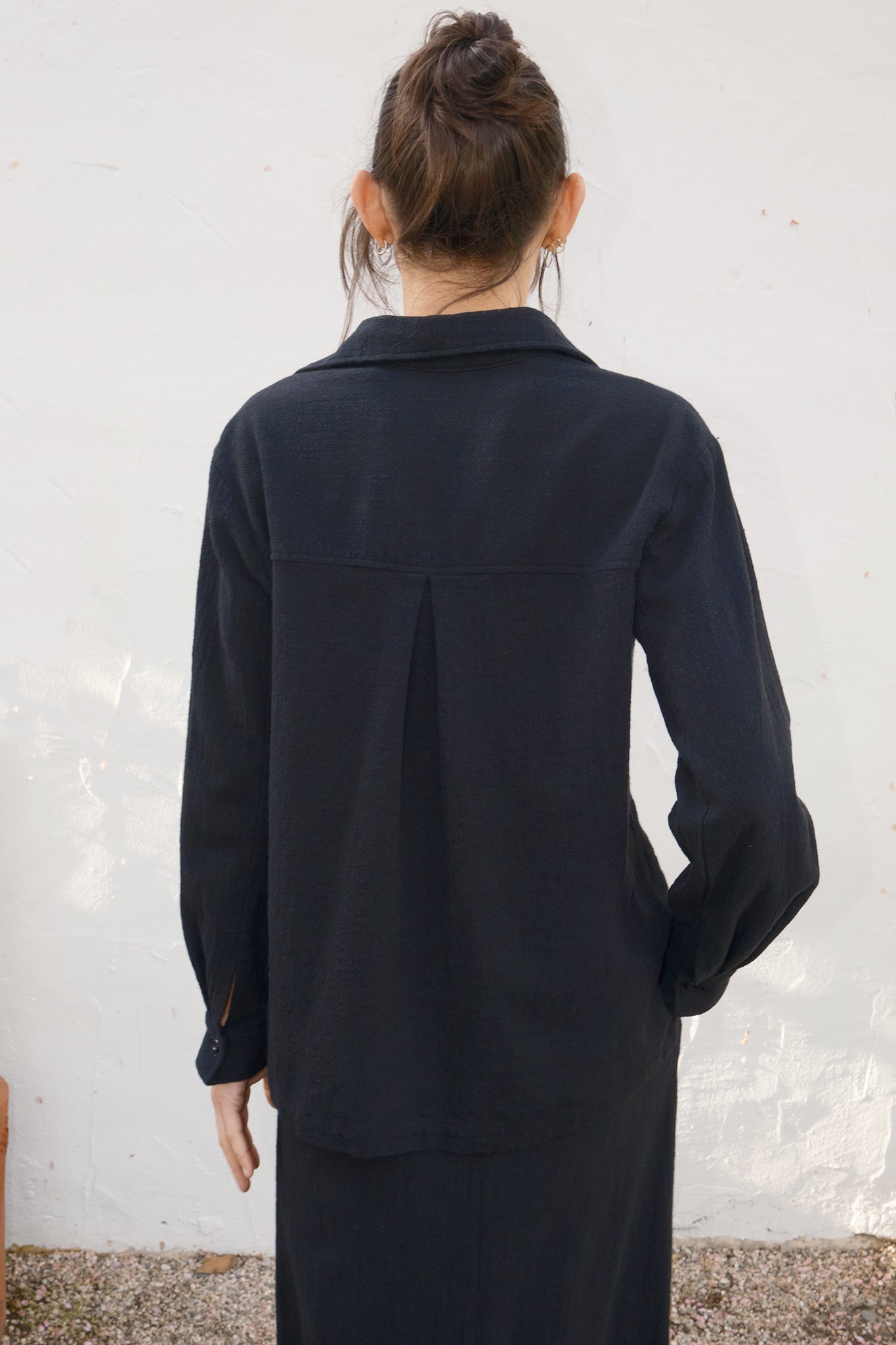 Person wearing a black outfit against a white wall
