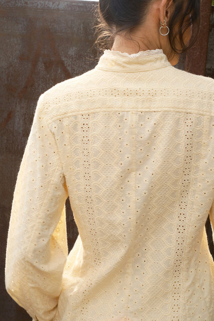 Close-up of a person wearing a cream-colored lace top against a blurred background