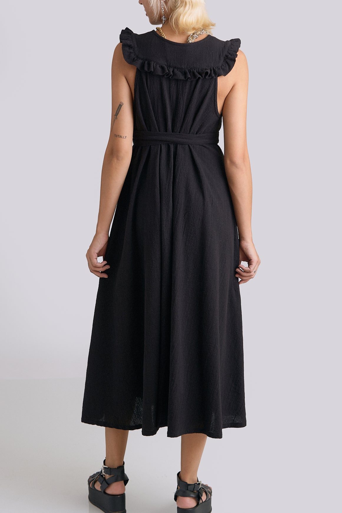 Black dress with ruffled collar worn by a person on a plain background