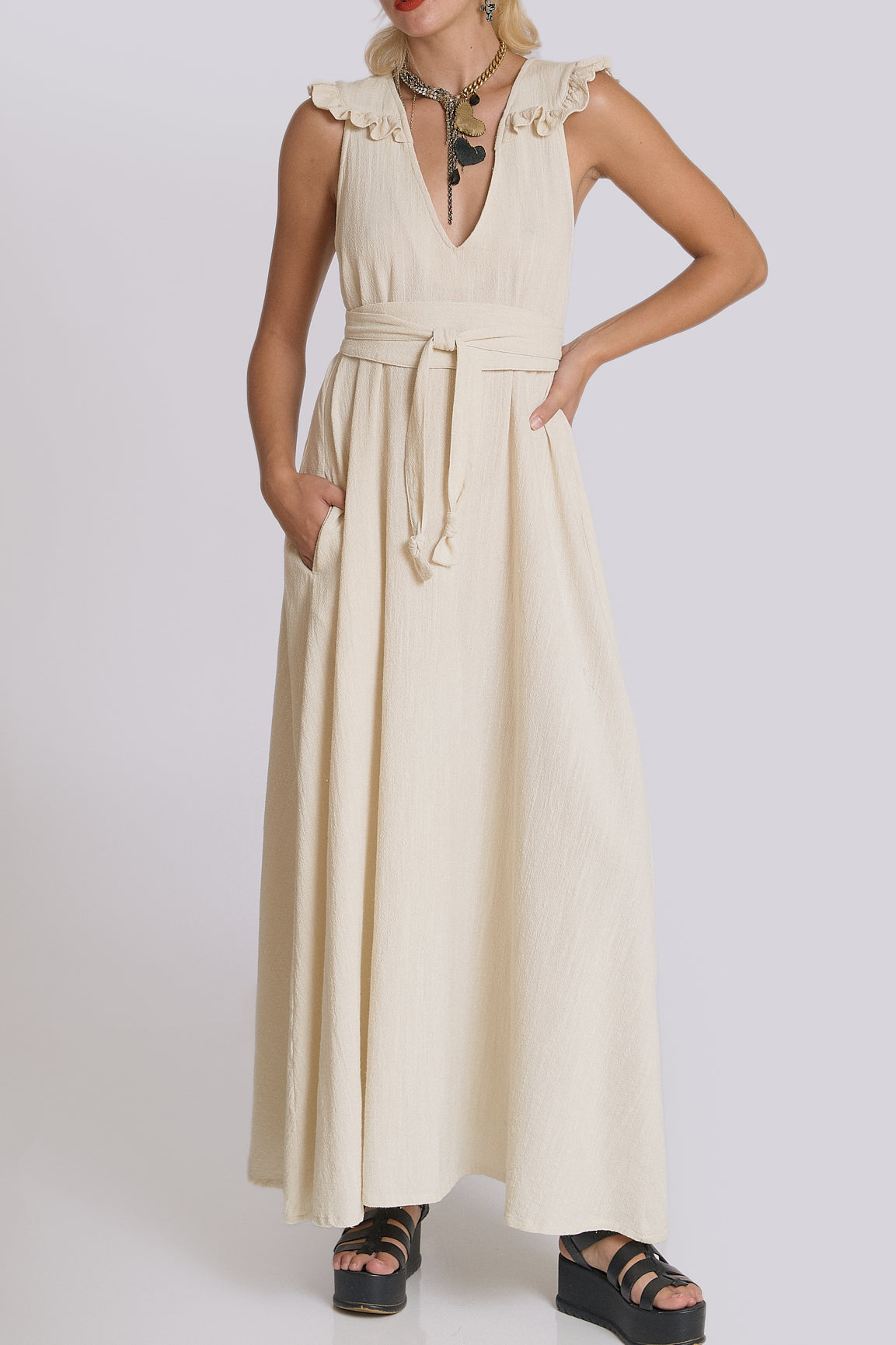 Woman wearing a beige sleeveless dress with a belt on a white background