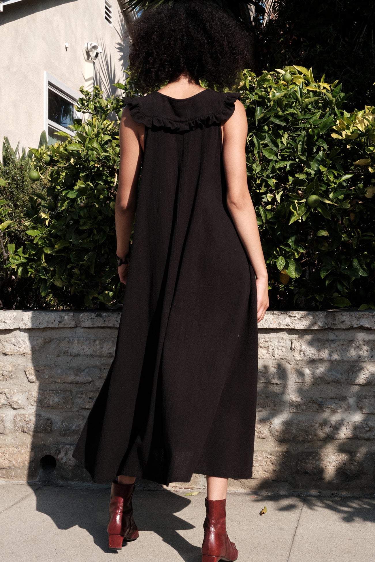 Person wearing a black dress with ruffled collar standing outdoors.