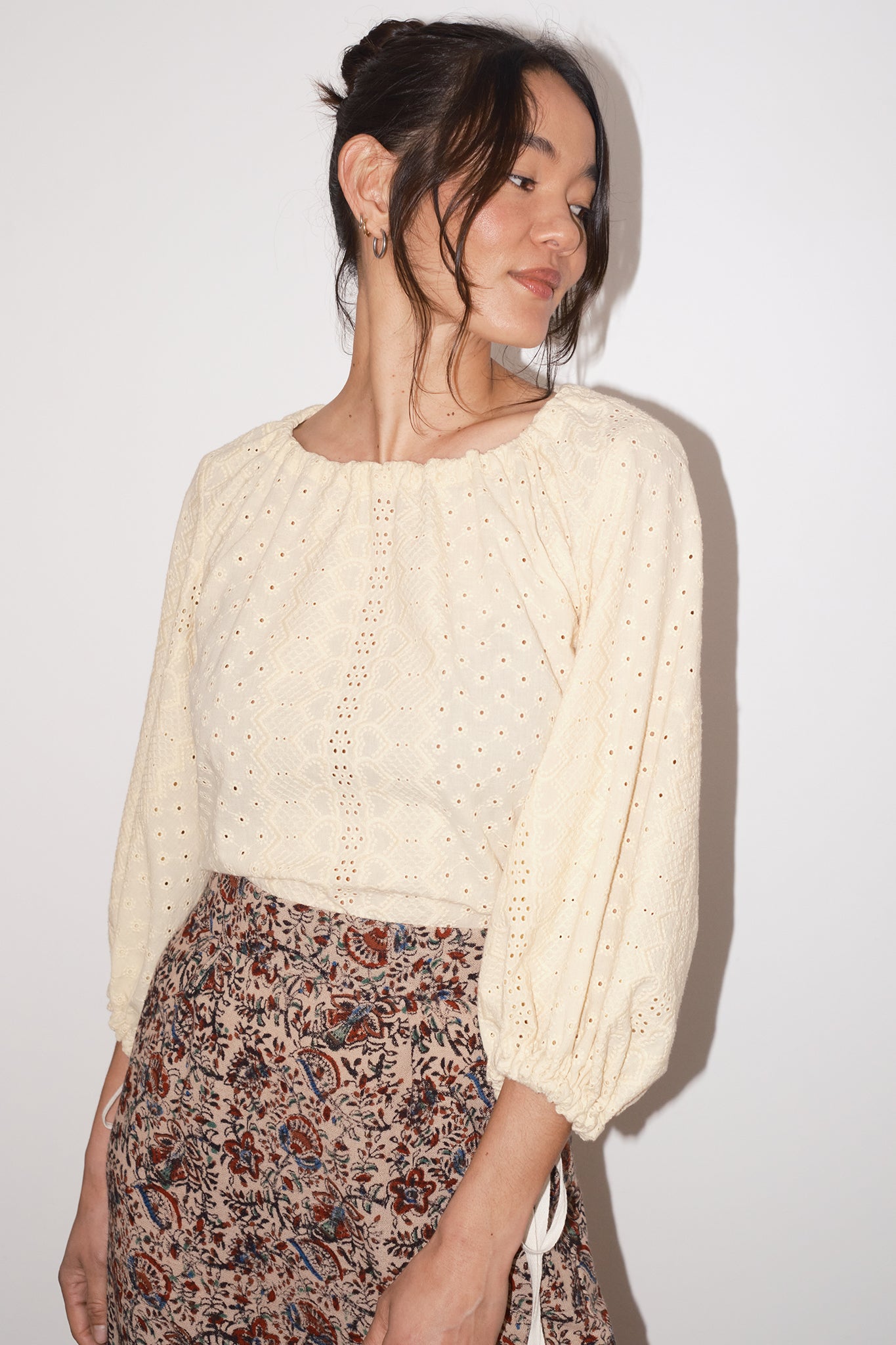 Woman wearing a cream-colored blouse with long sleeves and a patterned skirt against a white background