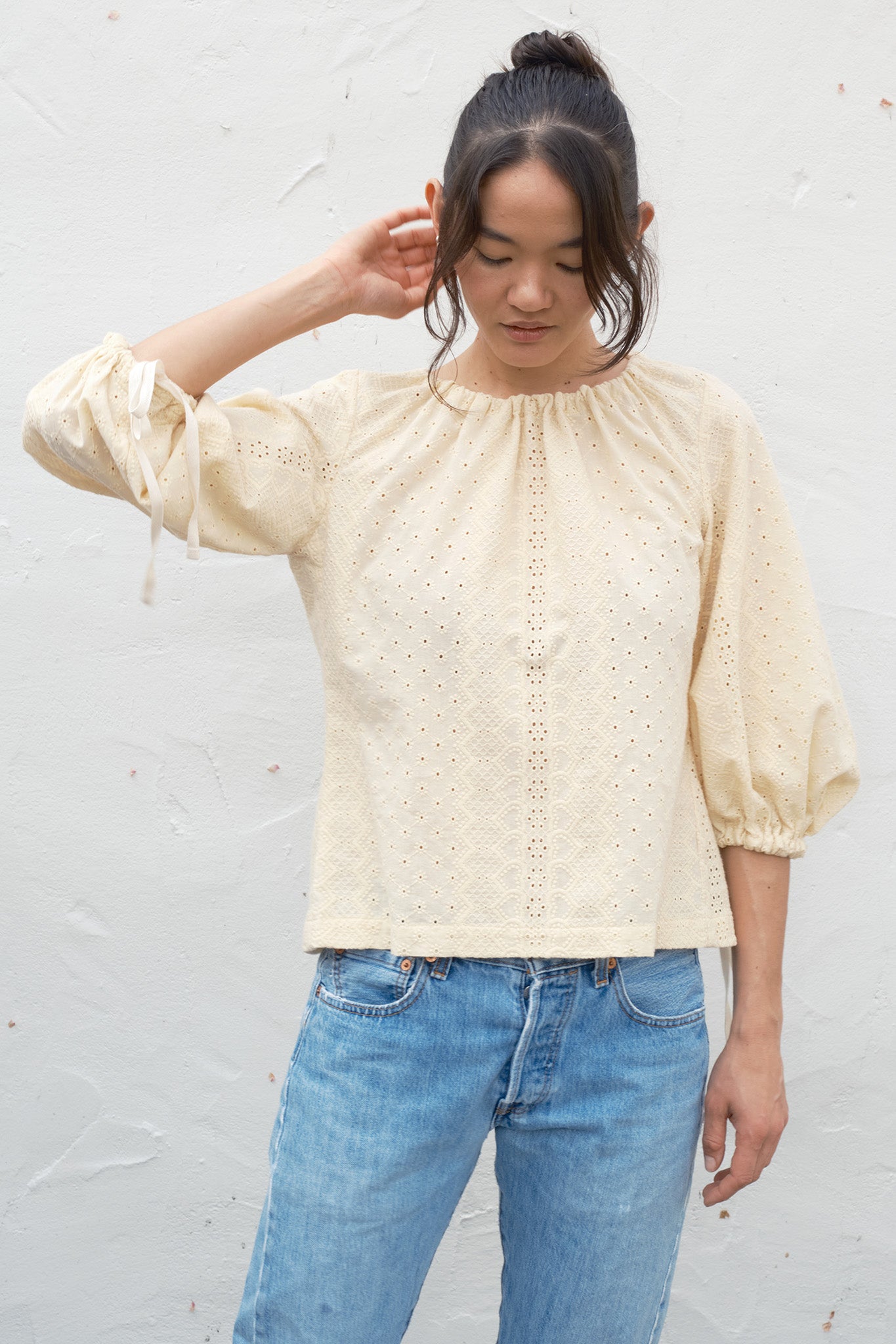Woman wearing a beige blouse with lace details and blue jeans against a white background
