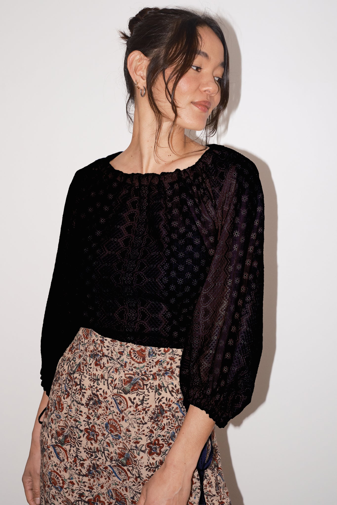Woman wearing a black patterned top and floral skirt against a white background