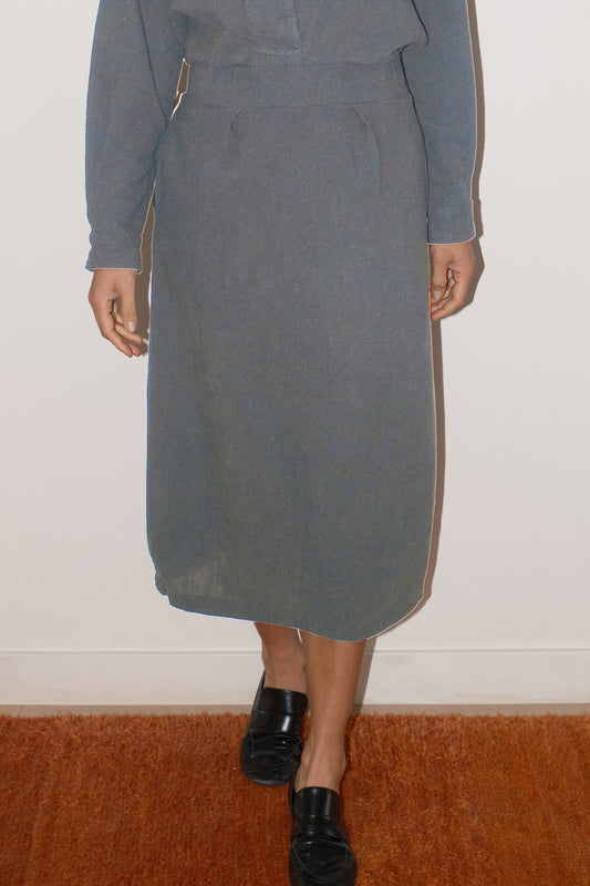 Person wearing a gray skirt with a white wall background