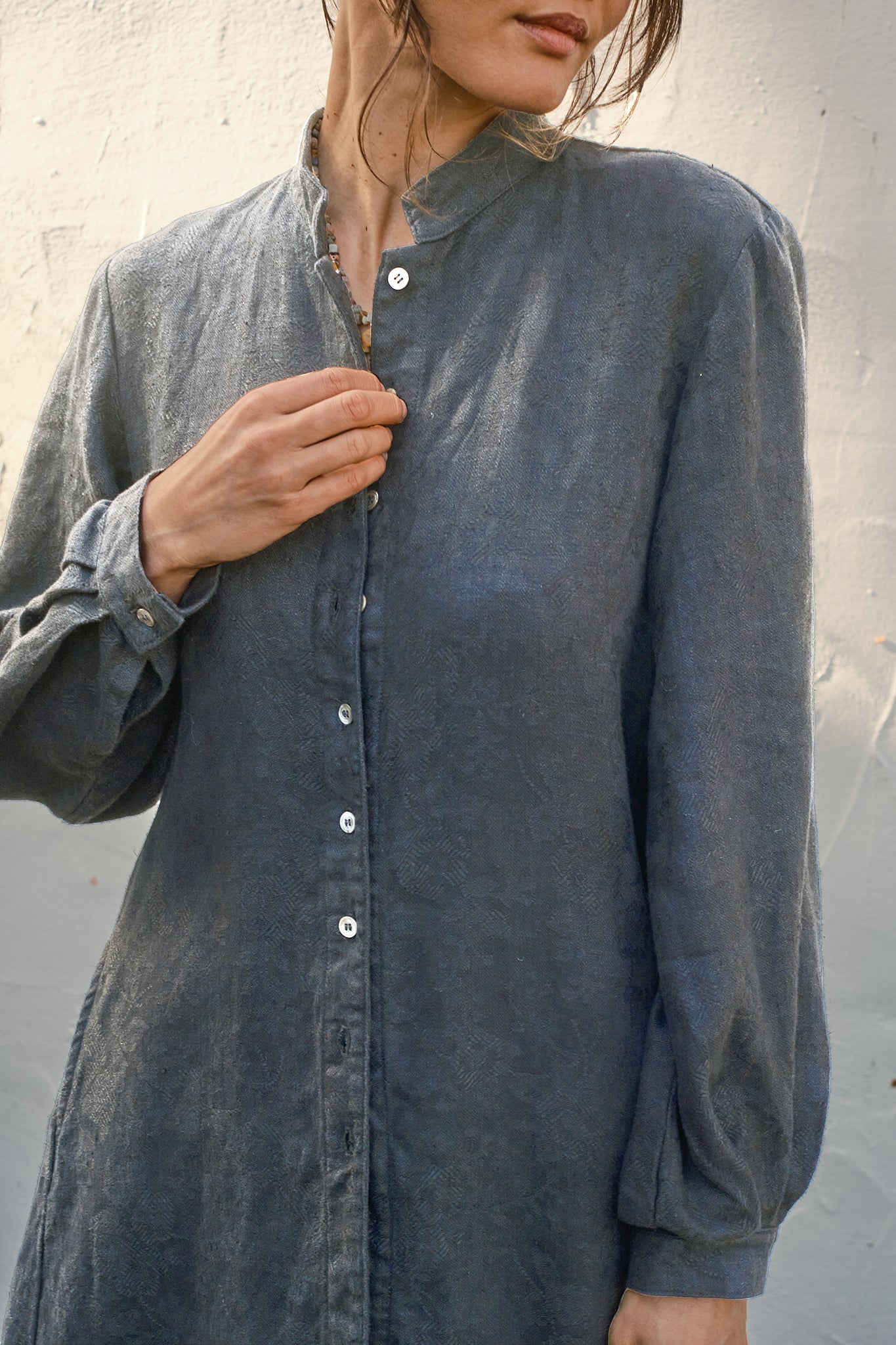 Detail of a person wearing a long, pewter coat against a neutral background