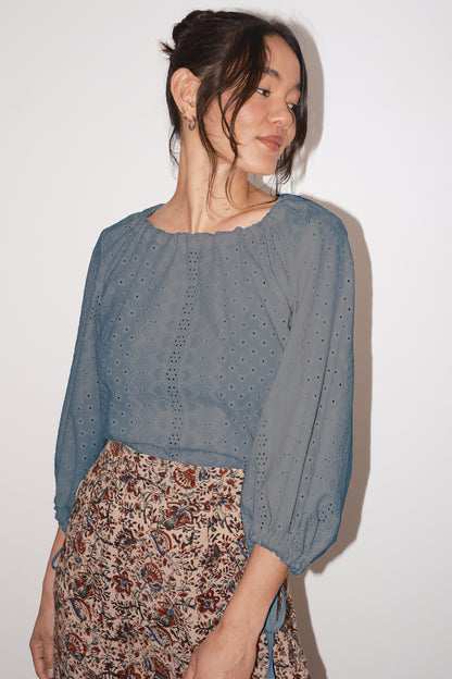 Woman wearing a pewter blouse with floral skirt against a white background