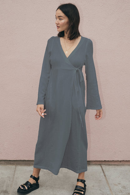 Woman wearing a gray wrap dress against a pink wall.