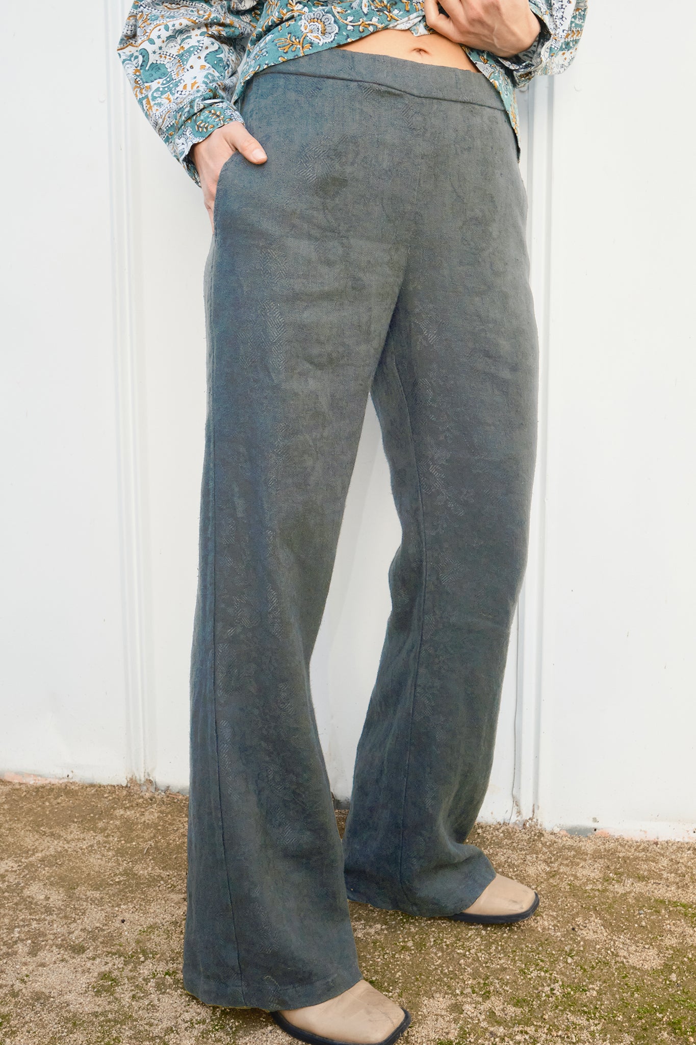 Person wearing grey flared pants against a white wall.